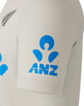Close-up of cream polo showing blue ANZ logo on the sleeve and Castore branding on the chest.