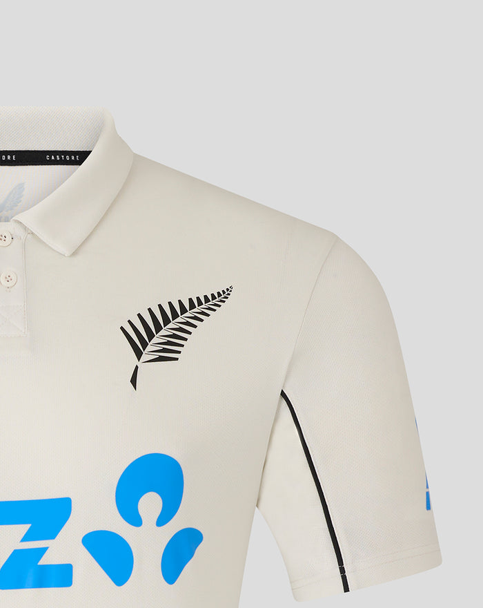 Cream short sleeve polo shirt with black fern logo on the left chest and blue graphic motifs.