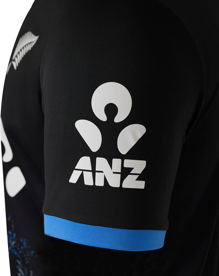 Black short sleeve shirt close up showing white ANZ logo on the sleeve and a blue cuff band